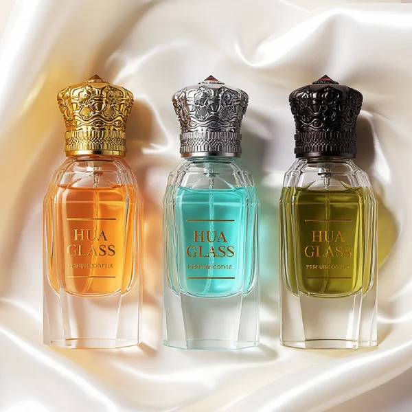 Three clear glass perfume bottles with faceted, angular bodies and heavy, thick bases are shown containing amber, light blue, and olive green liquids. Each bottle is topped with an ornate, highly detailed Zamac crown-motif cap featuring intricate filigree metalwork and a small red pointed gem accent at the peak, presented in polished gold, bright silver, and dark gunmetal finishes.