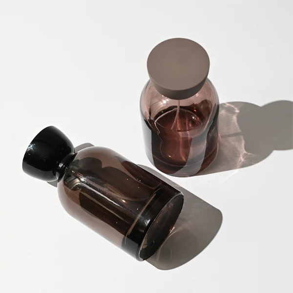 HUA0412 perfume bottle, luxury rounded oval glass bottle with translucent deep multi-color finish in brown, grey, red, or blue, featuring a printed gold logo and a unique glossy black tapered cup-shaped wooden or plastic cap, modern elegant fragrance packaging design available in 30ml, 50ml, and 100ml