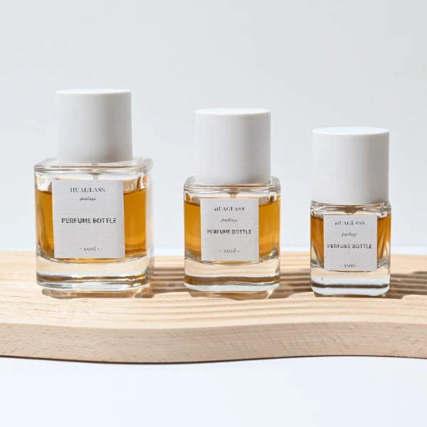 HUA0003 perfume bottles, sleek cylindrical clear glass with glossy black and white caps, golden-amber fragrance, timeless contemporary design, 30ml 50ml 100ml.