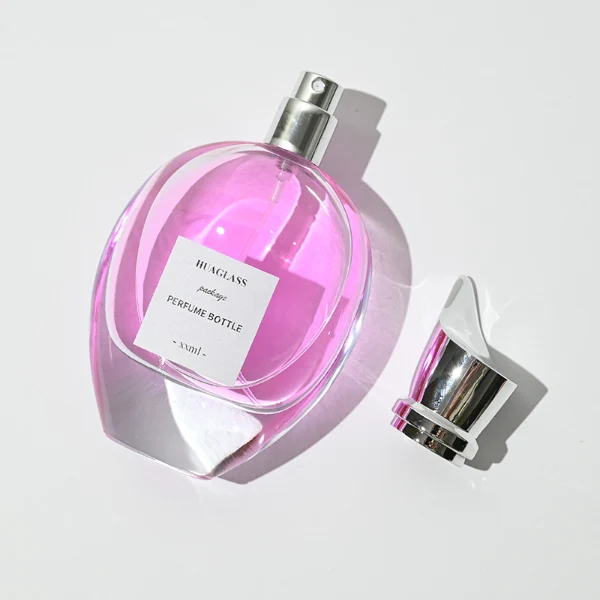 HUA0059 perfume bottle, heavy-base oval teardrop glass bottle with clear finish, featuring a square paper label, a matching neck, and a tall sculptural cylindrical plastic cap with a sharply angled sloping top in a smooth high-gloss shiny finish, elegant modern fragrance packaging design available in 30ml, 50ml, 75ml, and 100ml