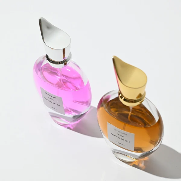 HUA0059 perfume bottle, heavy-base oval teardrop glass bottle with clear finish, featuring a square paper label, a matching neck, and a tall sculptural cylindrical plastic cap with a sharply angled sloping top in a smooth high-gloss shiny finish, elegant modern fragrance packaging design available in 30ml, 50ml, 75ml, and 100ml