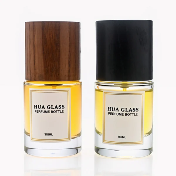 HUA0296 perfume bottle, cylindrical transparent colorless glass body with thick base and smooth rounded silhouette, 30 ml, 50 ml, or 100 ml liquid, cylindrical wooden cap in natural wood or matte black finish, printed label attached on bottle surface, modern minimalist luxury design, ideal for gifting and daily use.