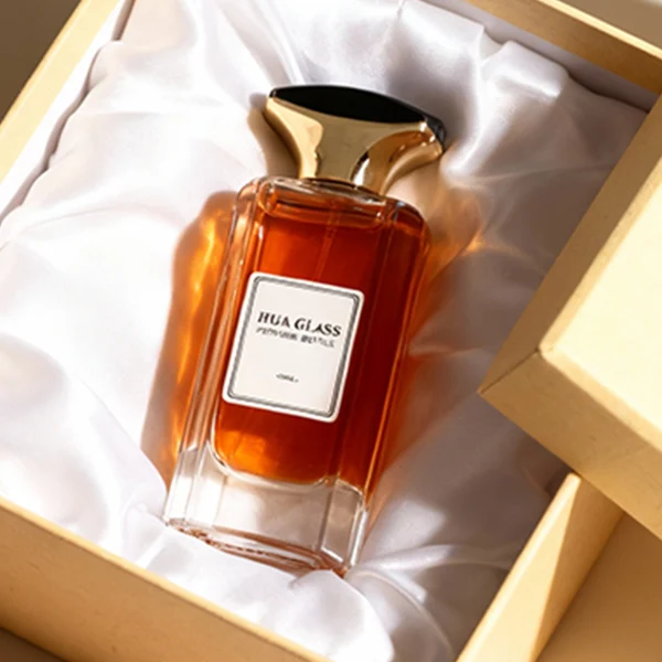HUA0384 perfume bottle, flat rectangular cuboid clear glass body with beveled edges and centered paper label, unique dual-tone funnel-shaped plastic cap with glossy black top and gold body, luxury fragrance packaging design available in 50ml and 100ml
