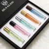 HUA0407 perfume bottle, slim cylindrical glass travel atomizer with tinted semi-transparent multi-color glass body in smoky black, orange or green featuring a subtle brand logo, topped with a luxury gold or black cylindrical zamak cap, modern minimalist travel fragrance packaging available in 10ml